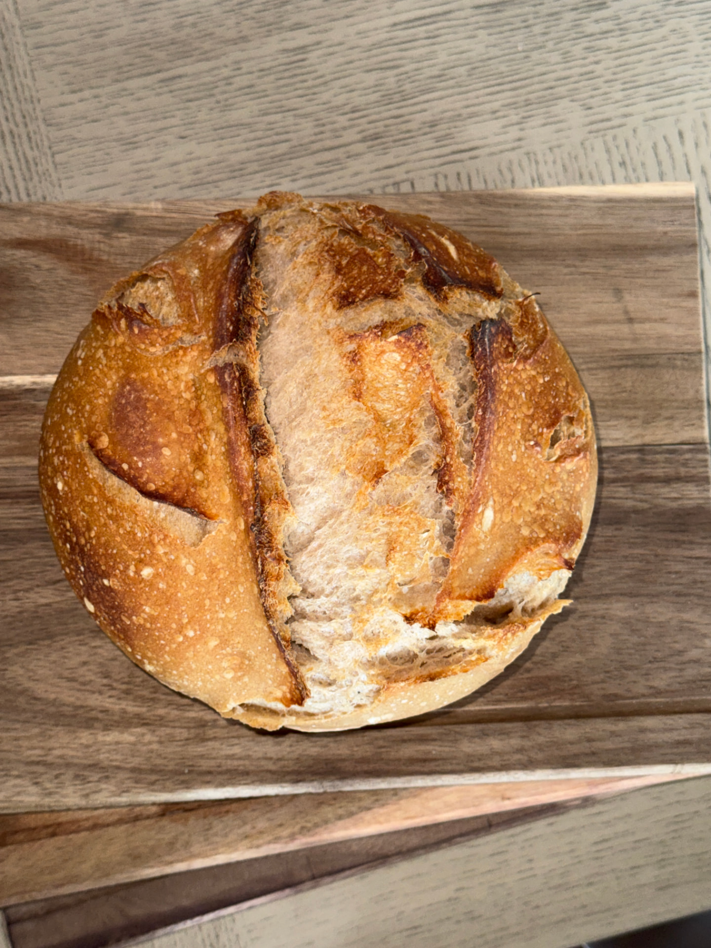 Golden scored sourdough boule resting on a wooden cutting board