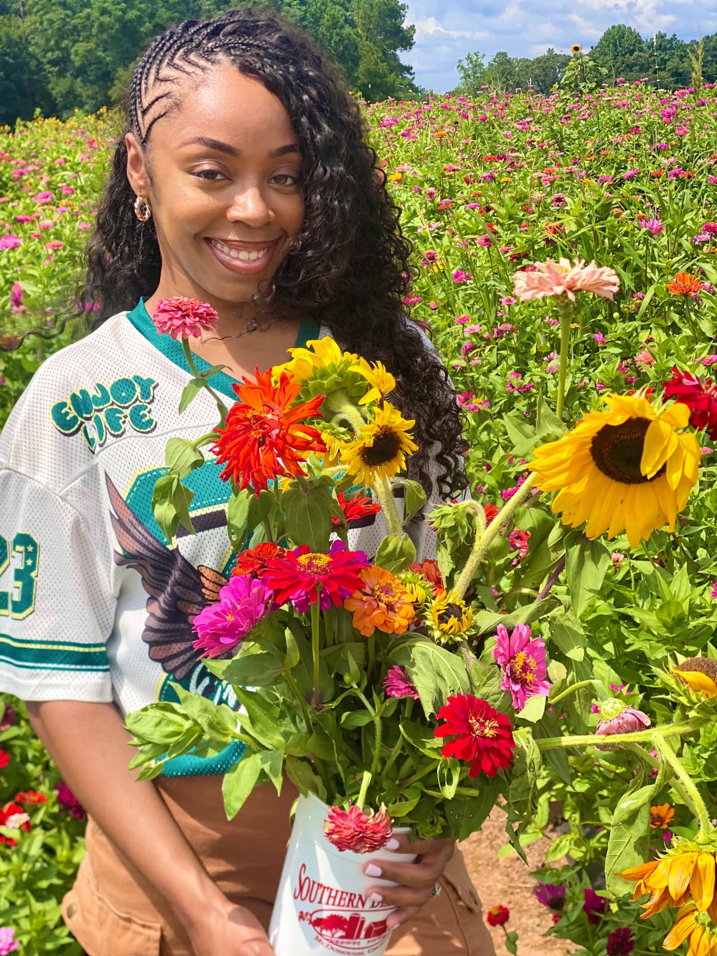 Woman holding a bucket of freshly cut zinnias and sunflowers in a flower field
